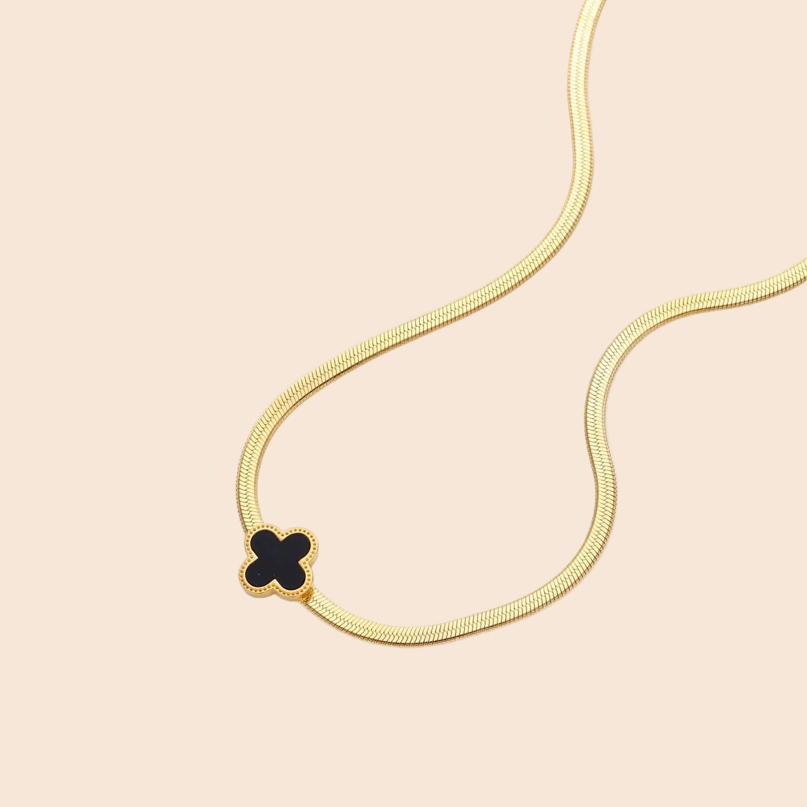 Dainty 18K gold-plated herringbone chain necklace with black enamel quatrefoil clover pendant on white background