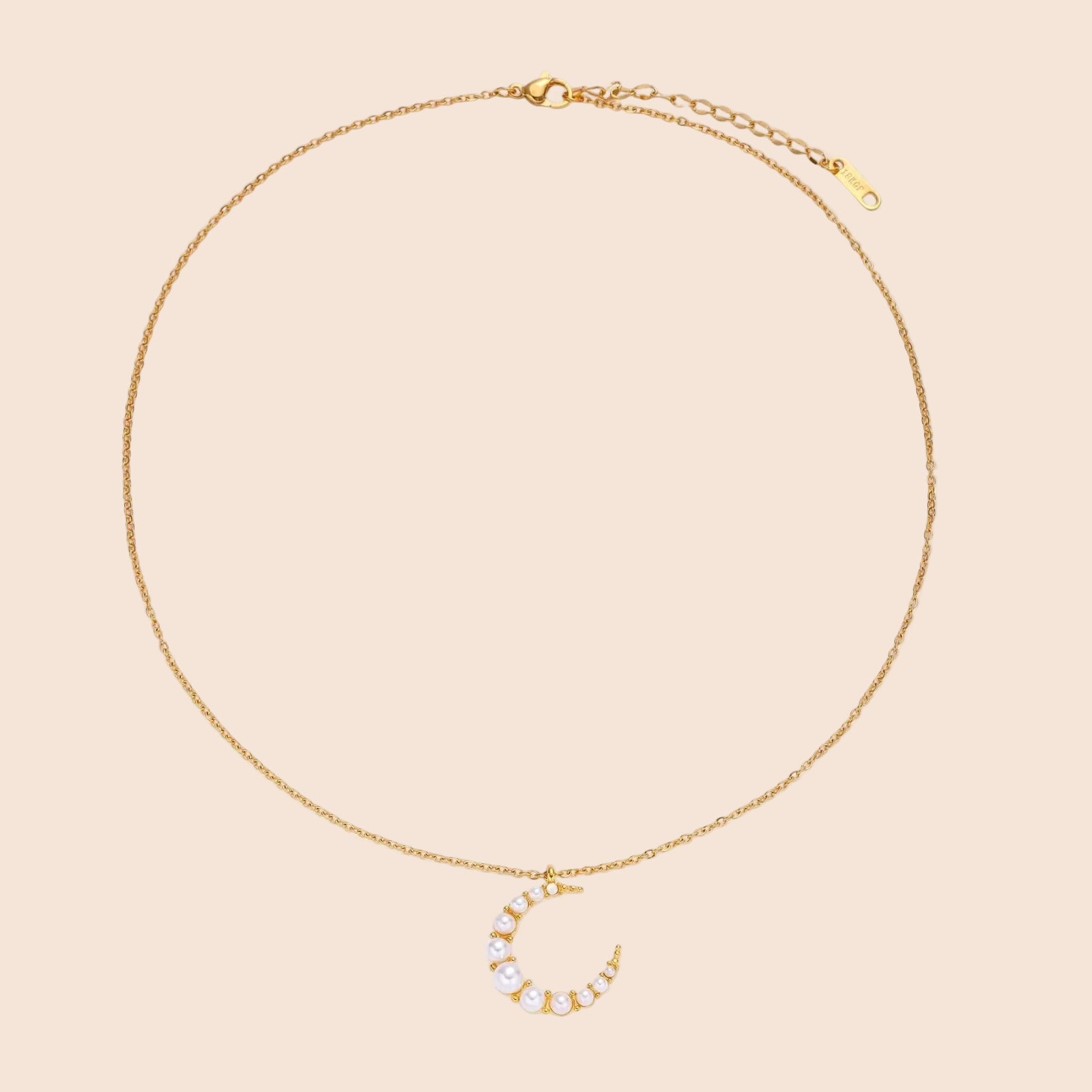 Gold crescent moon pendant with graduated white pearls on delicate chain against cream background