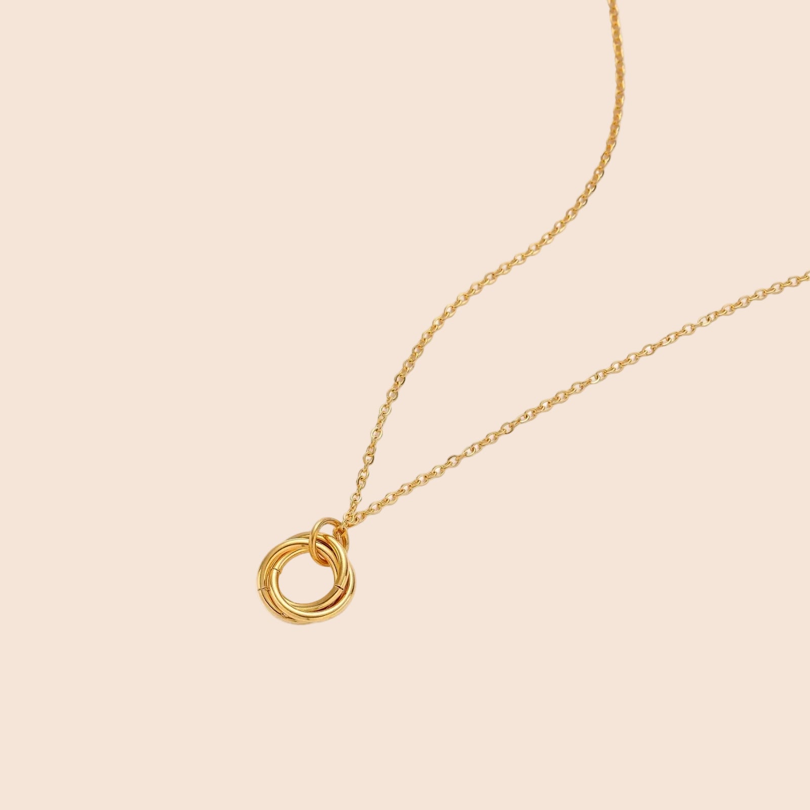 Delicate gold-plated necklace with three interlocking circle rings forming a minimalist knot pendant on cream background
