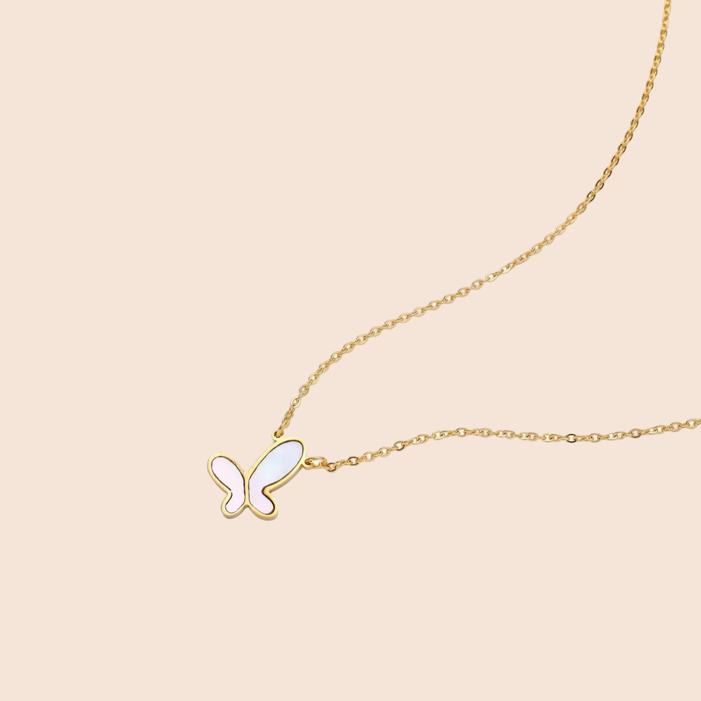 Gold-plated butterfly pendant with iridescent mother of pearl inlay on delicate chain against cream background.