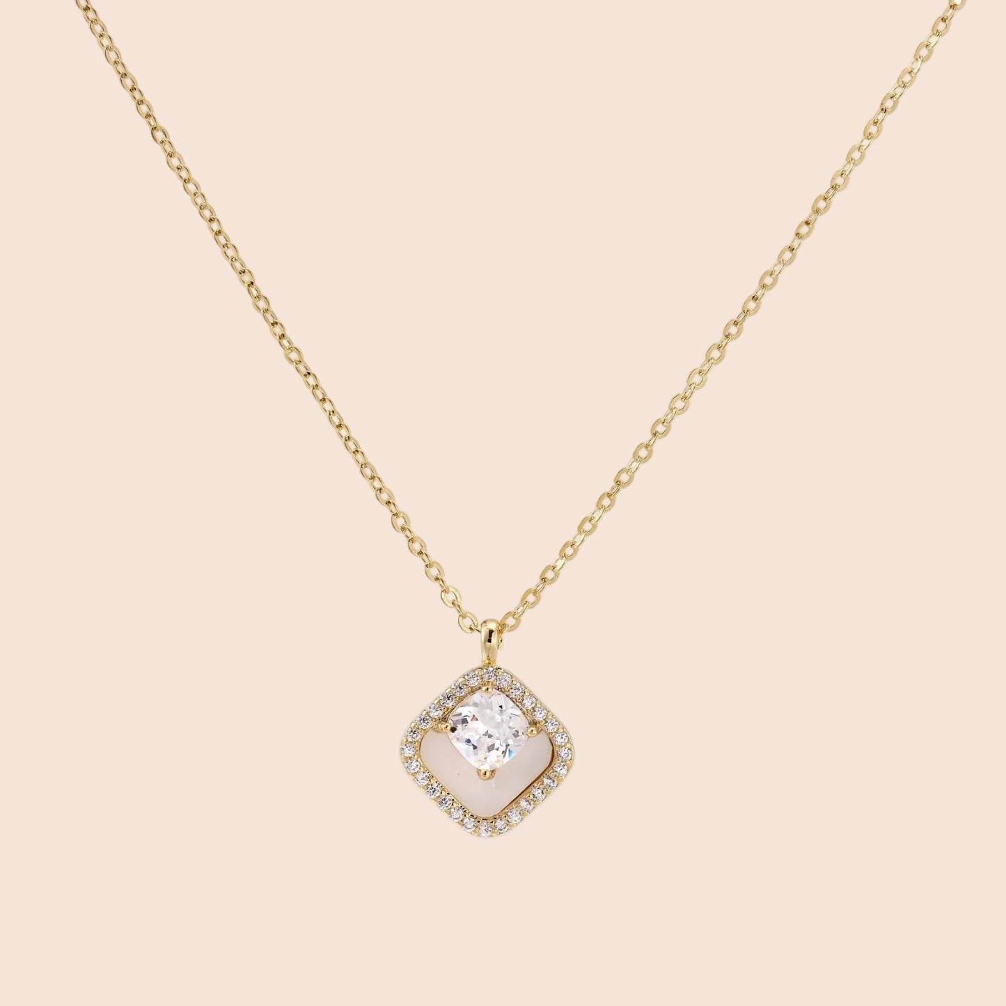 Gold quatrefoil pendant with crystal center on iridescent mother-of-pearl base, adjustable gold chain on cream background
