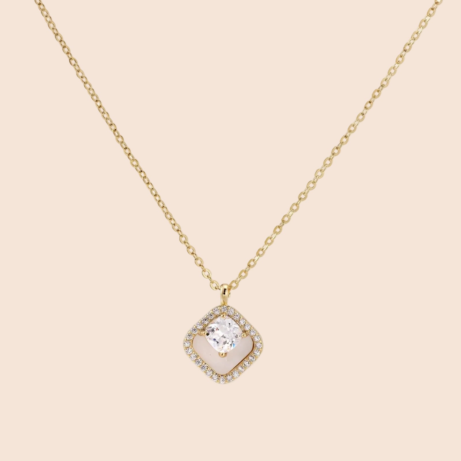 Gold quatrefoil pendant with crystal center on iridescent mother-of-pearl base, adjustable gold chain on cream background