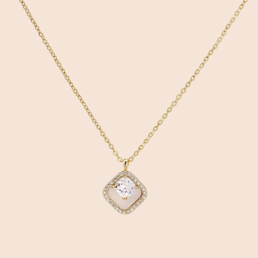 Gold quatrefoil pendant with crystal center on iridescent mother-of-pearl base, adjustable gold chain on cream background