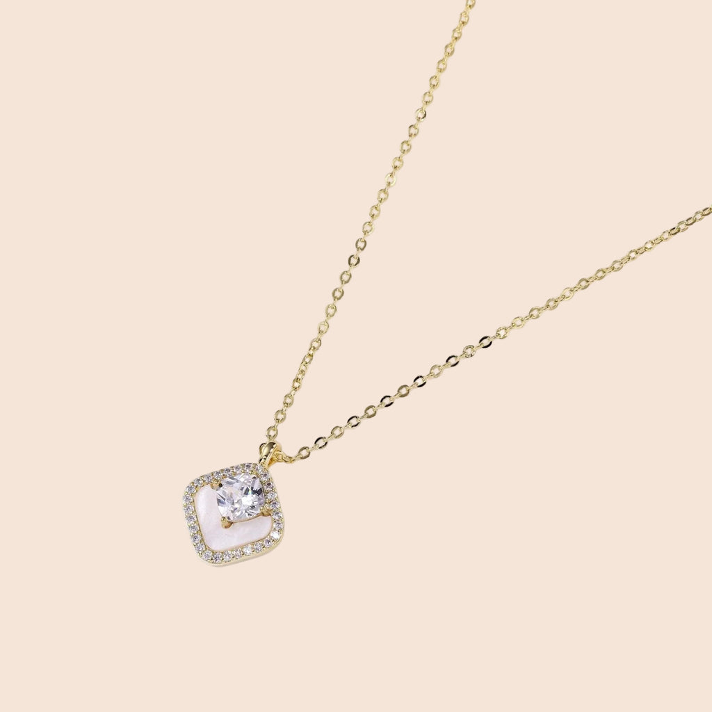 Gold quatrefoil pendant with crystal center on iridescent mother-of-pearl base, adjustable gold chain on cream background