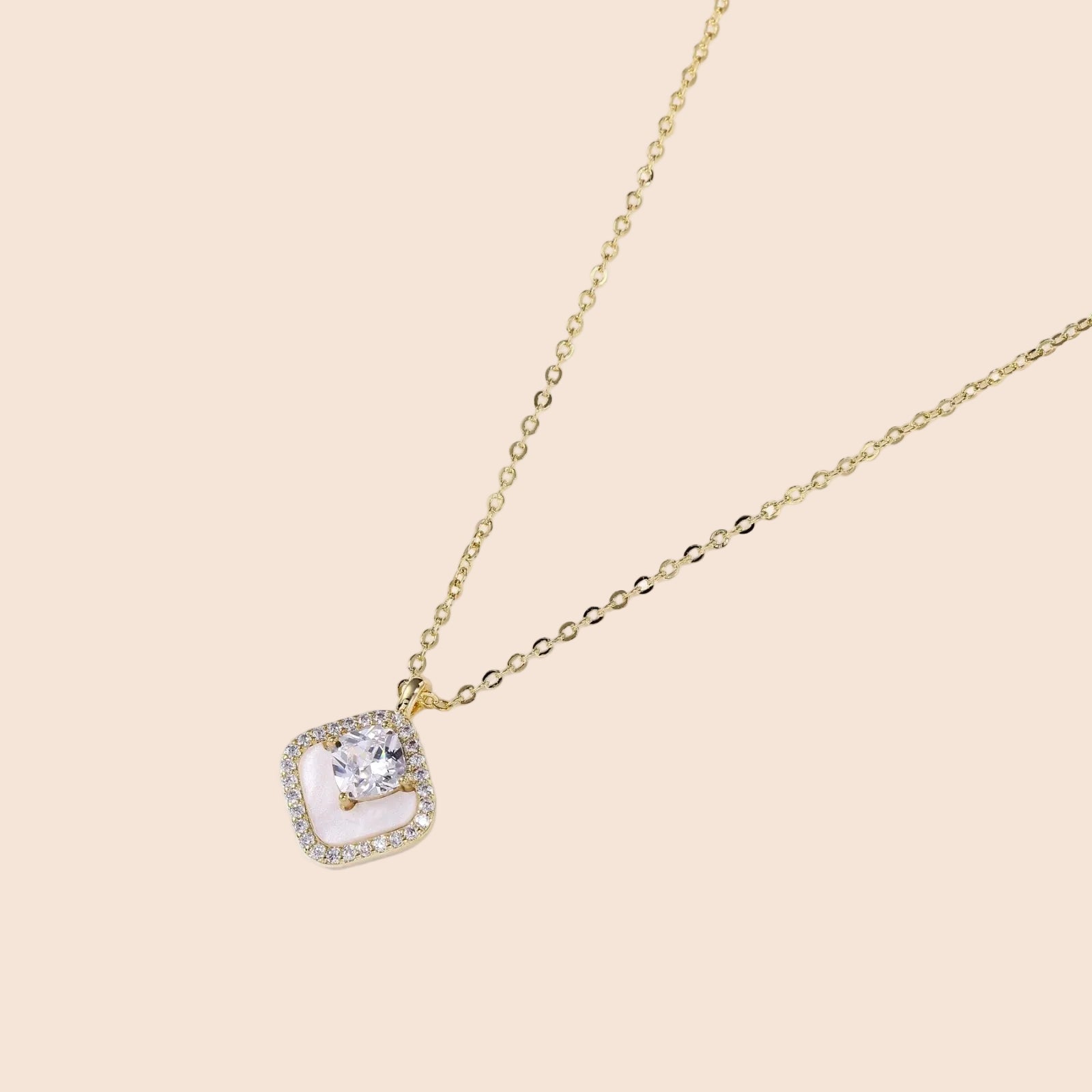 Gold quatrefoil pendant with crystal center on iridescent mother-of-pearl base, adjustable gold chain on cream background