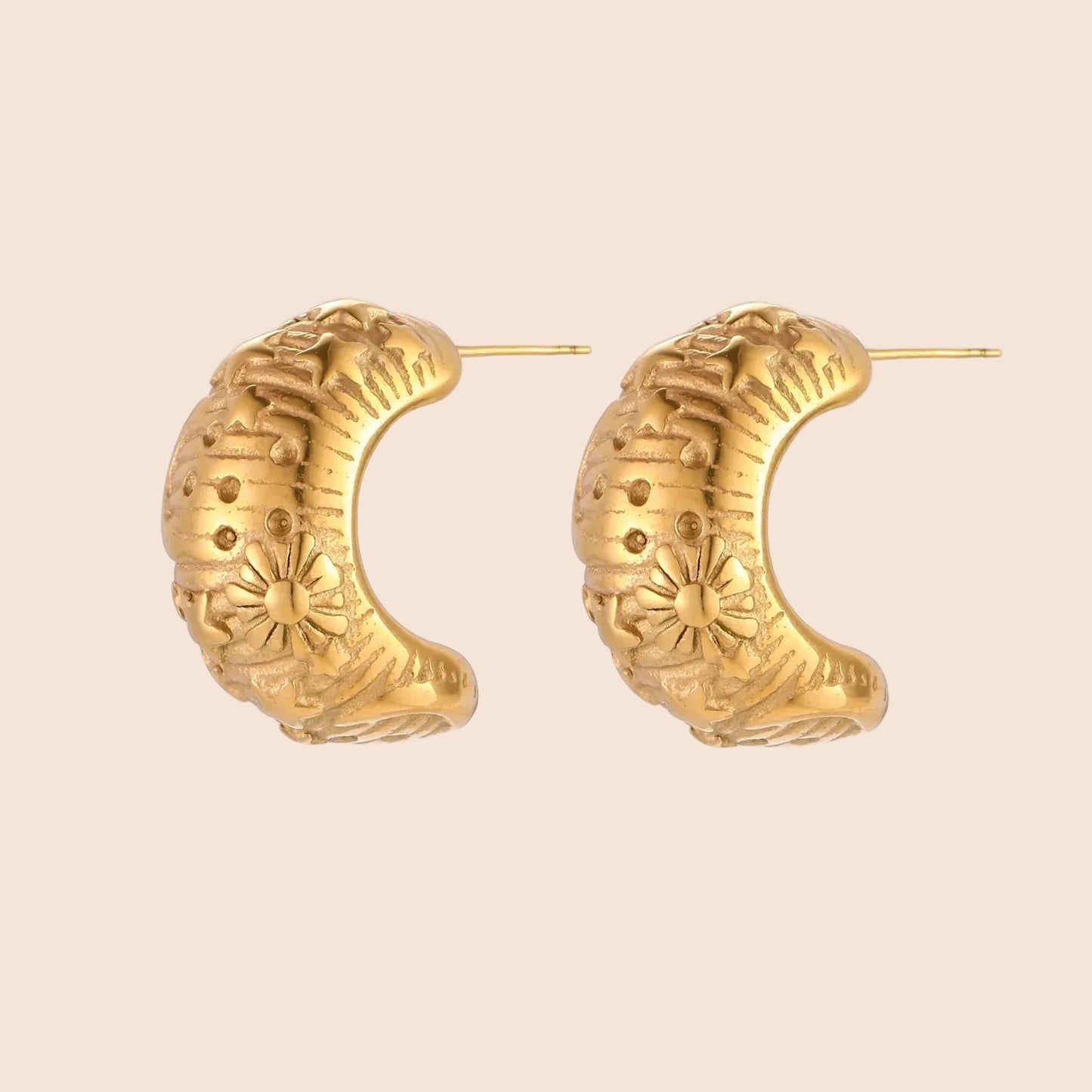 Gold-plated chunky hoop earrings with sun and star engravings on white background, showing detailed celestial pattern work.