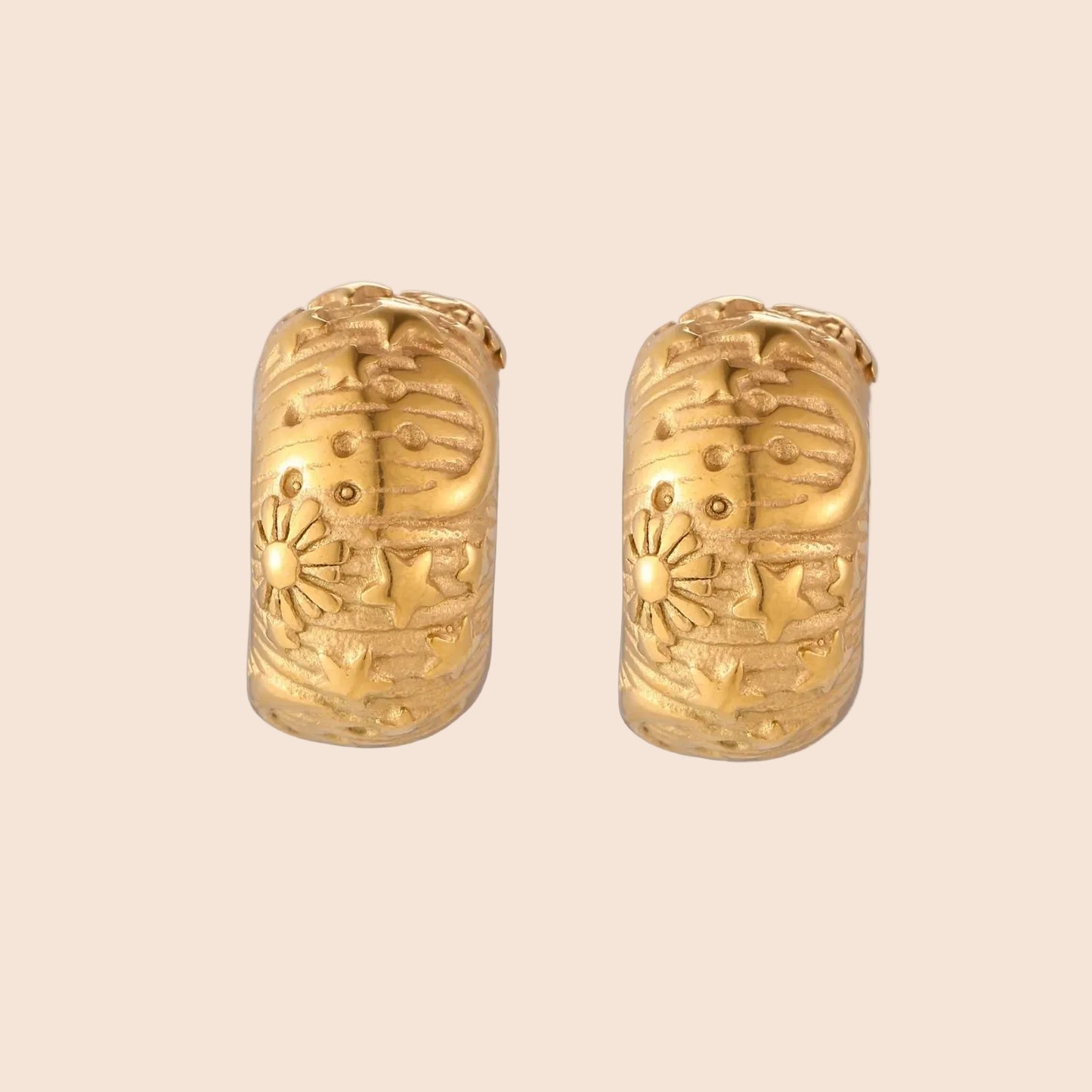 Gold-plated chunky hoop earrings with sun and star engravings on white background, showing detailed celestial pattern work.