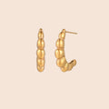 Gold-plated sculptural hoop earrings with chunky segmented design on cream background
