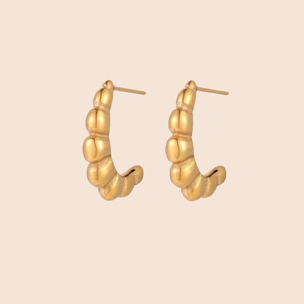 Gold-plated sculptural hoop earrings with chunky segmented design on cream background