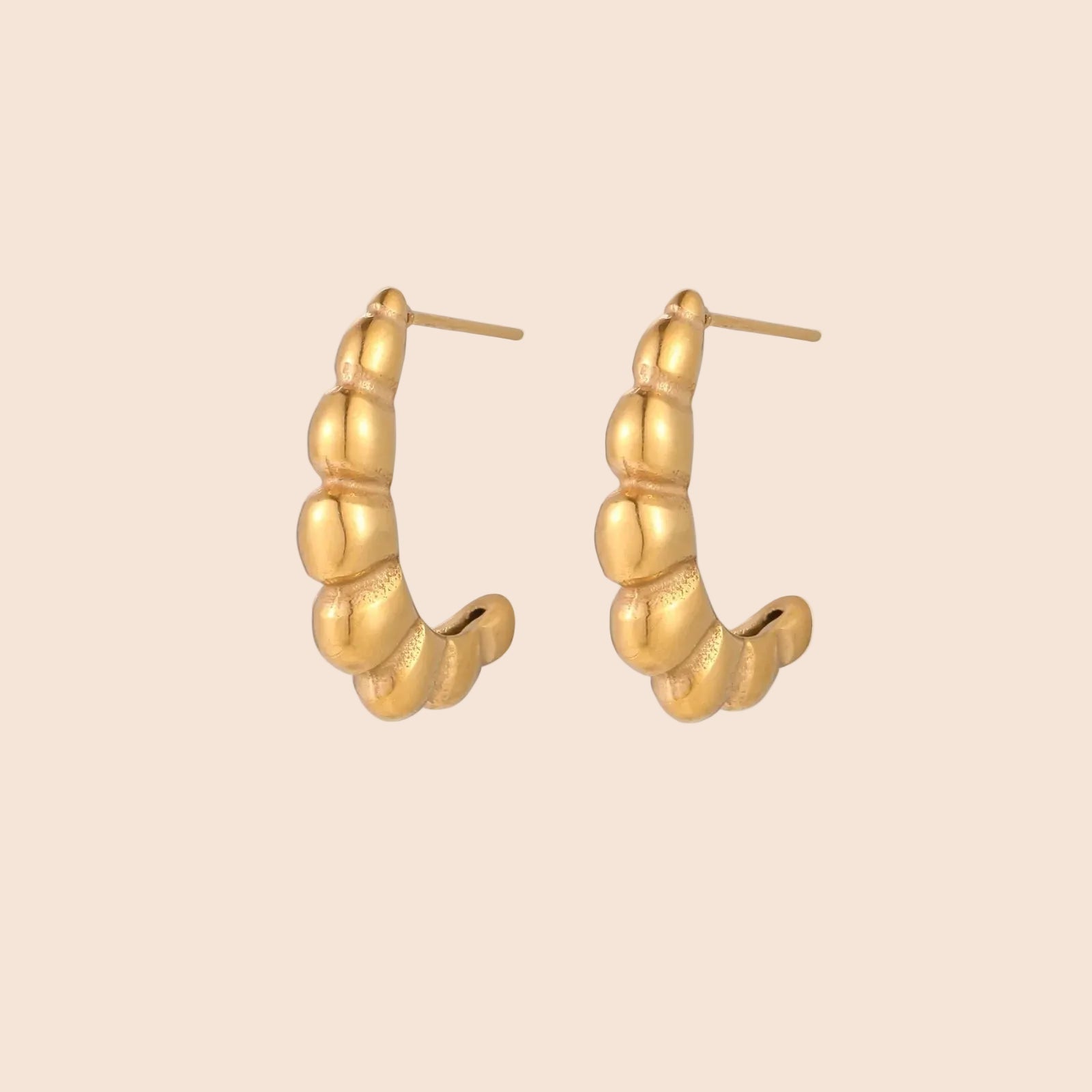 Gold-plated sculptural hoop earrings with chunky segmented design on cream background
