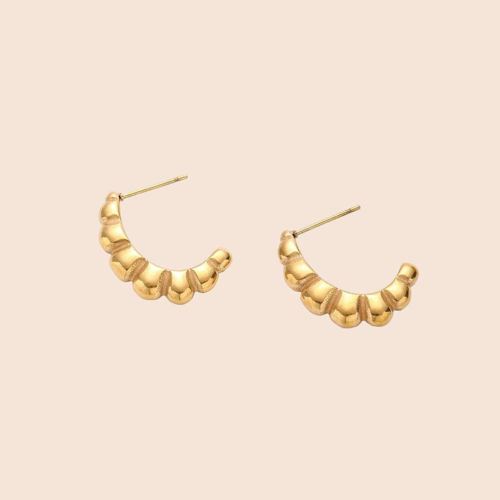 Gold-plated sculptural hoop earrings with chunky segmented design on cream background
