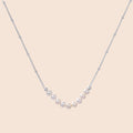Delicate sterling silver chain necklace with small freshwater pearls arranged in a curved smile arc on cream background.