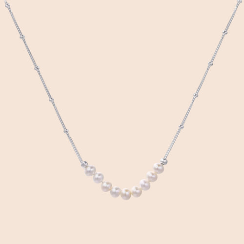Delicate sterling silver chain necklace with small freshwater pearls arranged in a curved smile arc on cream background.