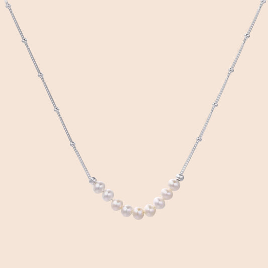 Delicate sterling silver chain necklace with small freshwater pearls arranged in a curved smile arc on cream background.