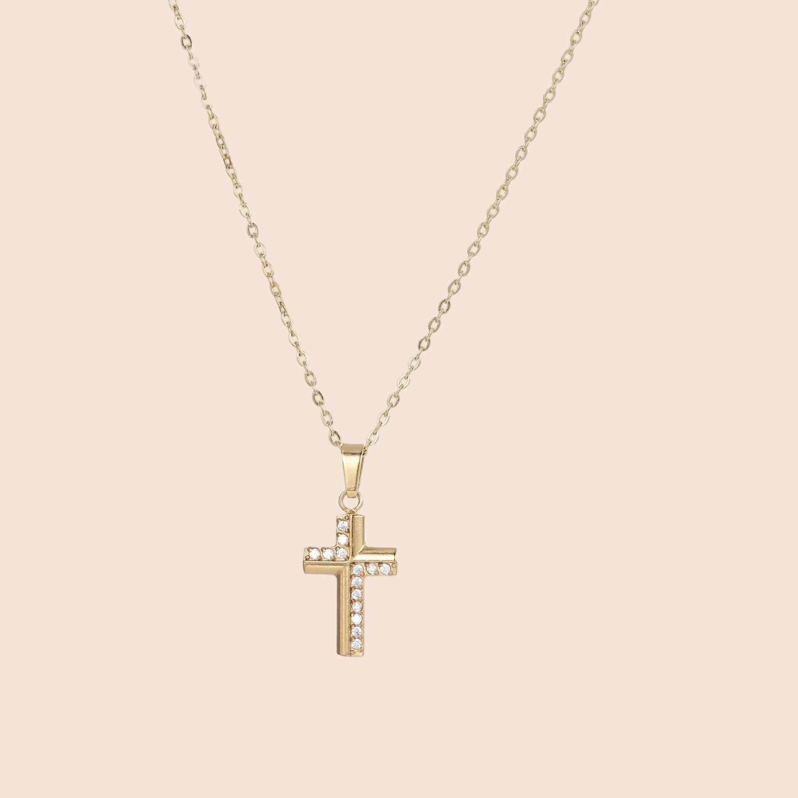 Delicate 14K gold-plated cross pendant with crystal accents on fine chain against cream background